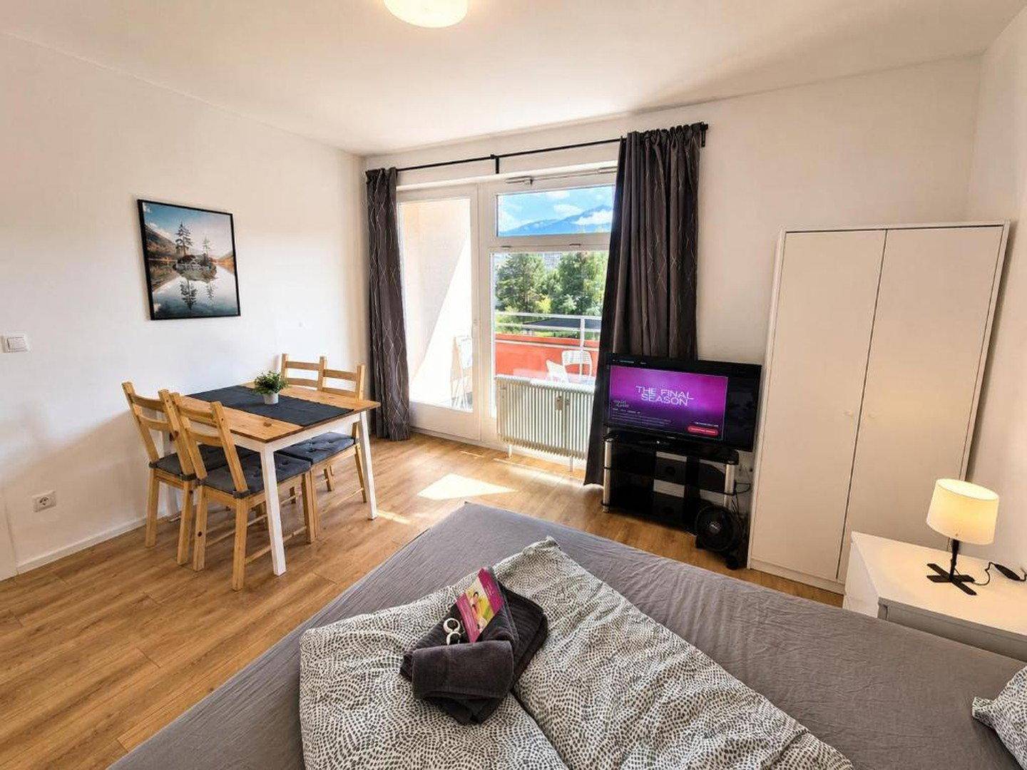 Kombinierter Wohn- und Essbereich mit Bett, Esstisch und Zugang zum Balkon mit Bergblick.