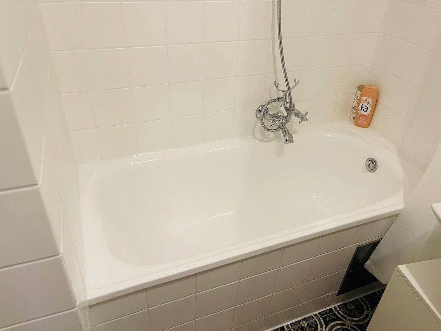 Eingebaute Badewanne mit weißen Wandfliesen und einem gemusterten Boden im Badezimmer.