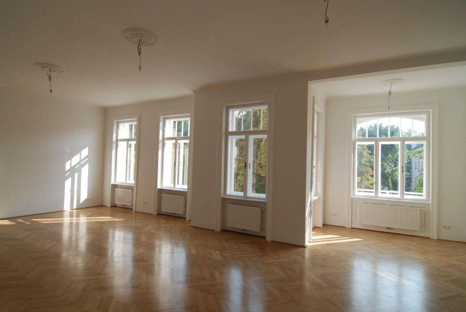 Großzügiger, lichtdurchfluteter Raum mit Fischgrätparkett, hohen Decken und Blick ins Grüne.