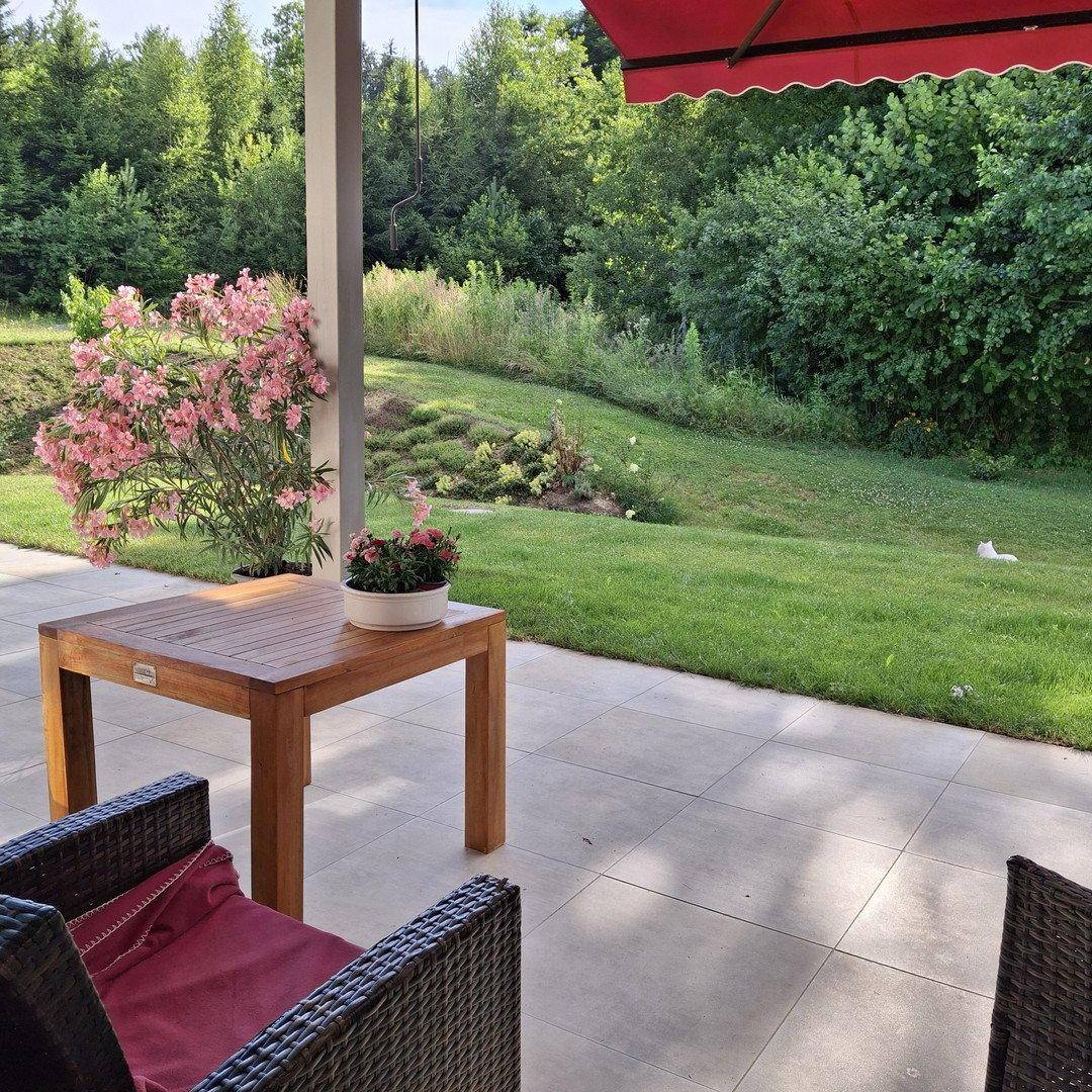 Gemütliche Terrasse mit Holztisch und Blick ins Grüne, umgeben von blühenden Pflanzen.