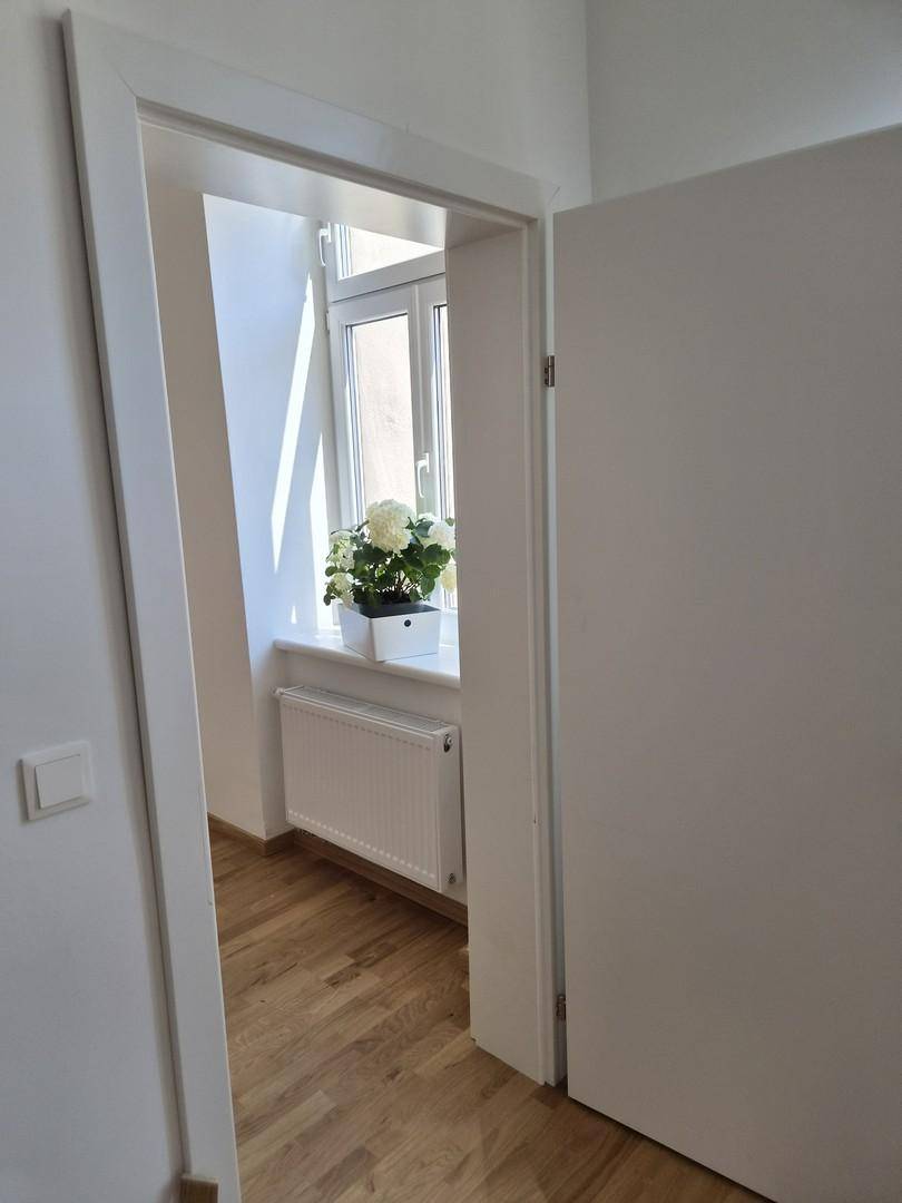 Heller Flur mit Holzboden und Fenster, dekoriert mit einer weißen Hortensie auf der Fensterbank.