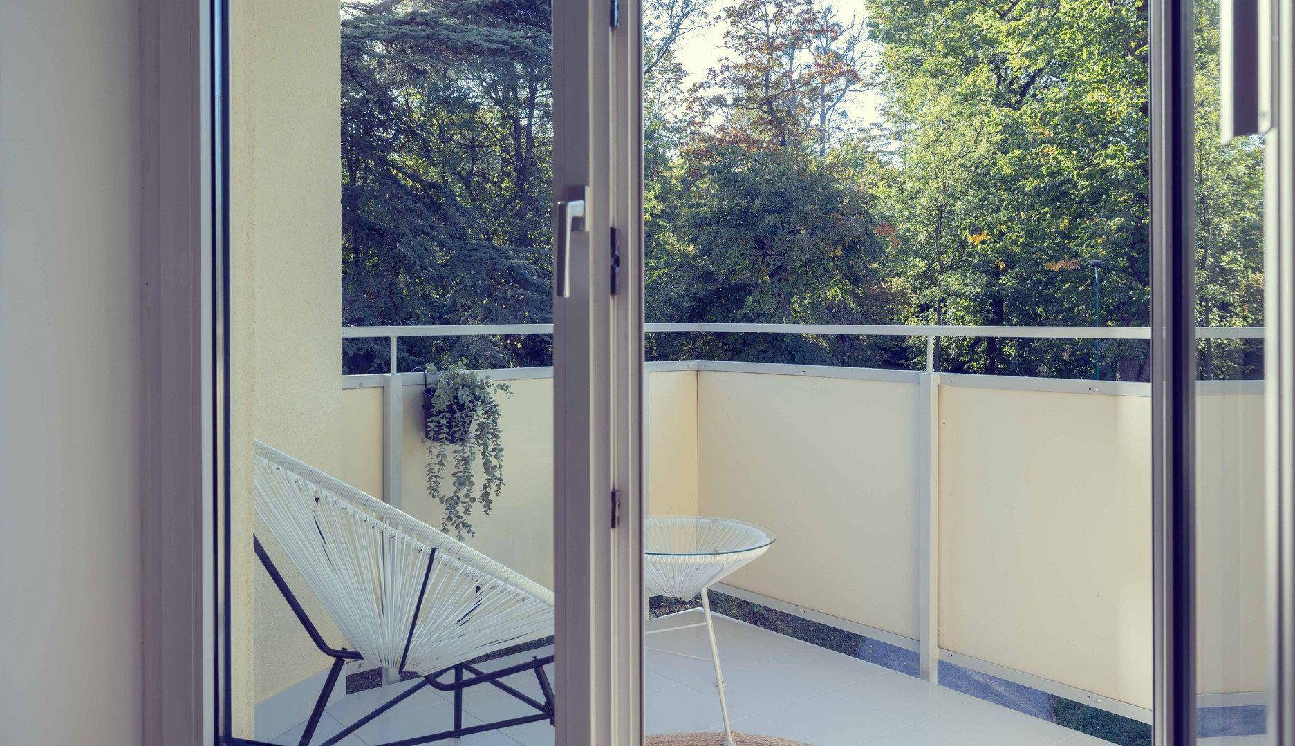 Heller Balkon mit Sitzgelegenheit und Blick auf grüne Bäume, ideal zum Entspannen.