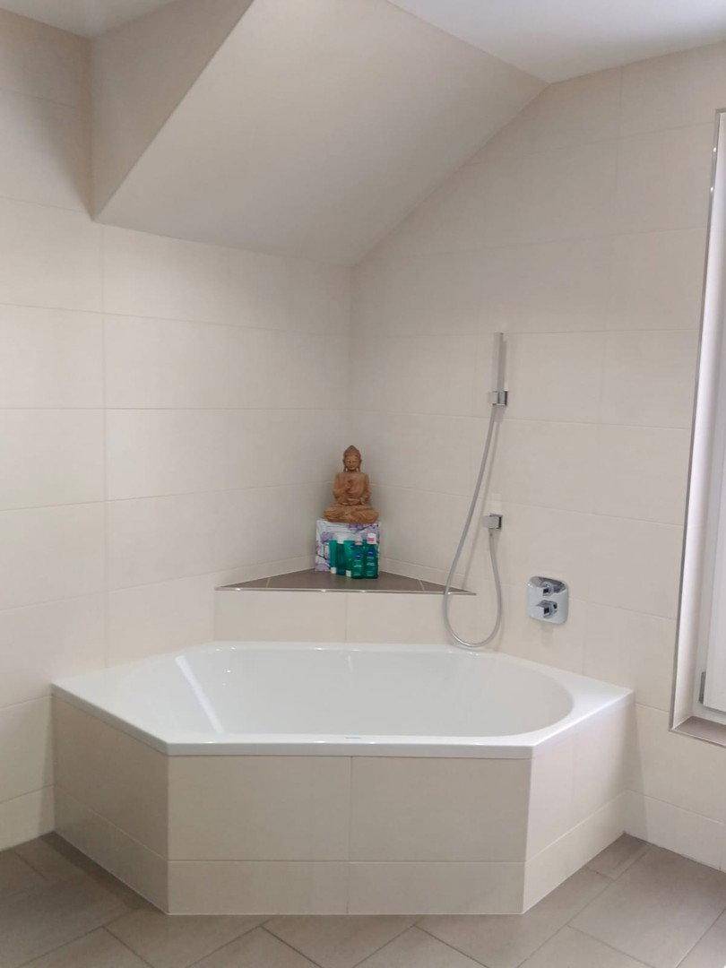 Eckbadewanne in einem hell gefliesten Badezimmer mit einer kleinen Buddha-Statue als Dekoration.