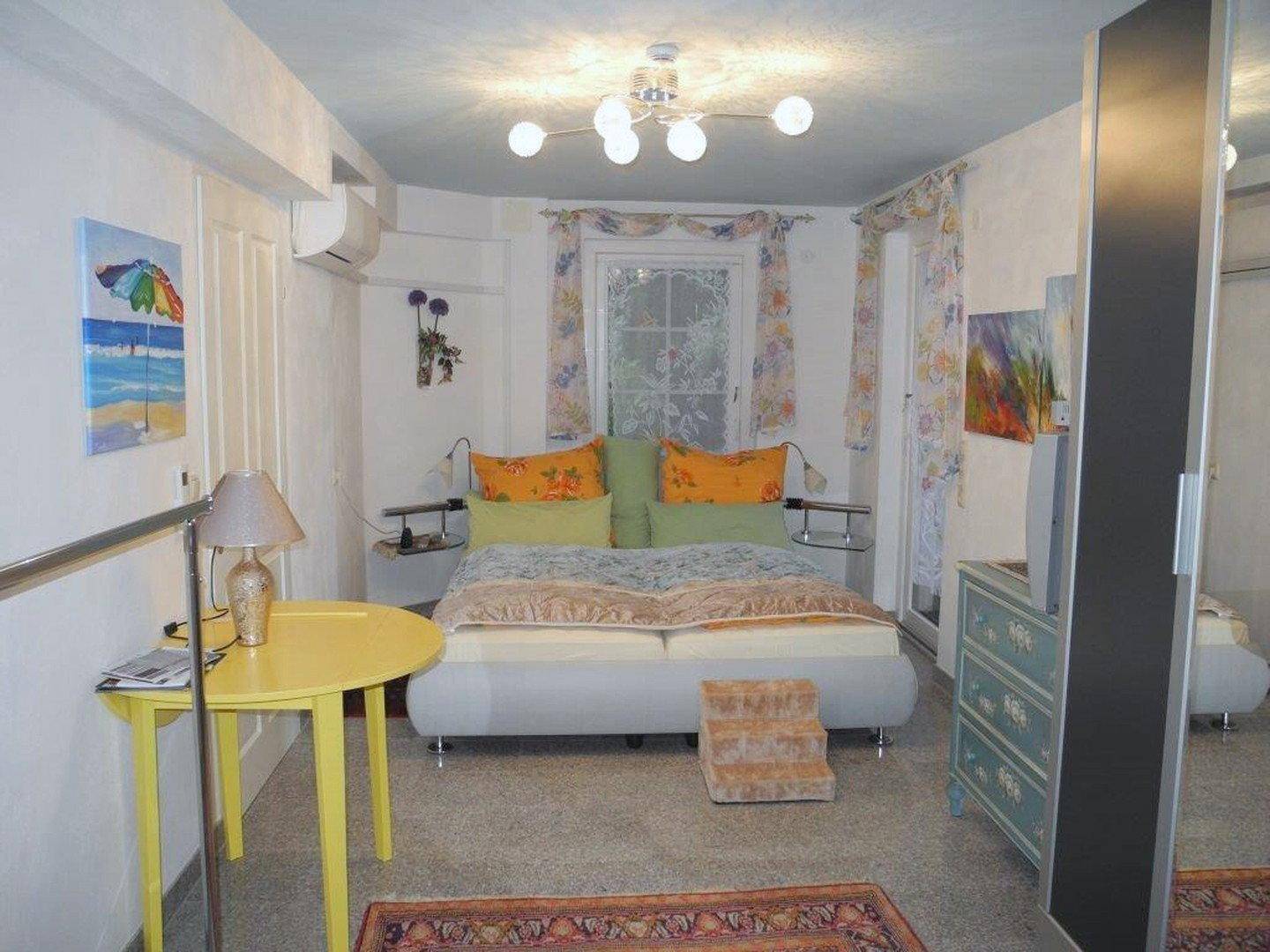 Schlafzimmer mit Doppelbett, Spiegel, farbenfroher Dekoration und Deckenventilator.