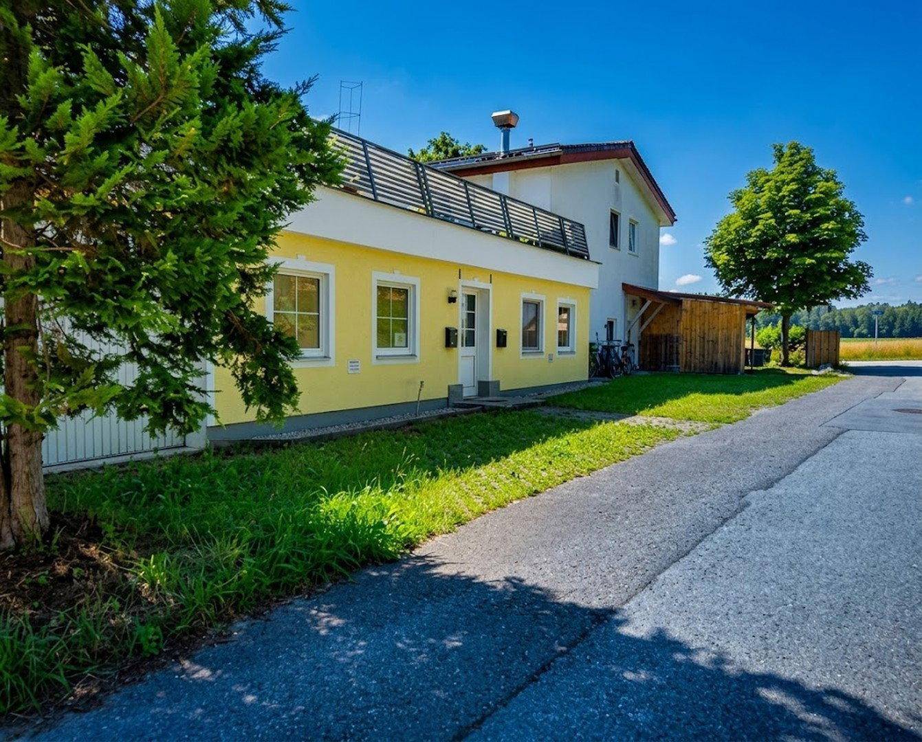Gelbes Gebäude mit weißem Obergeschoss, umgeben von grünem Rasen und einem gepflasterten Weg.