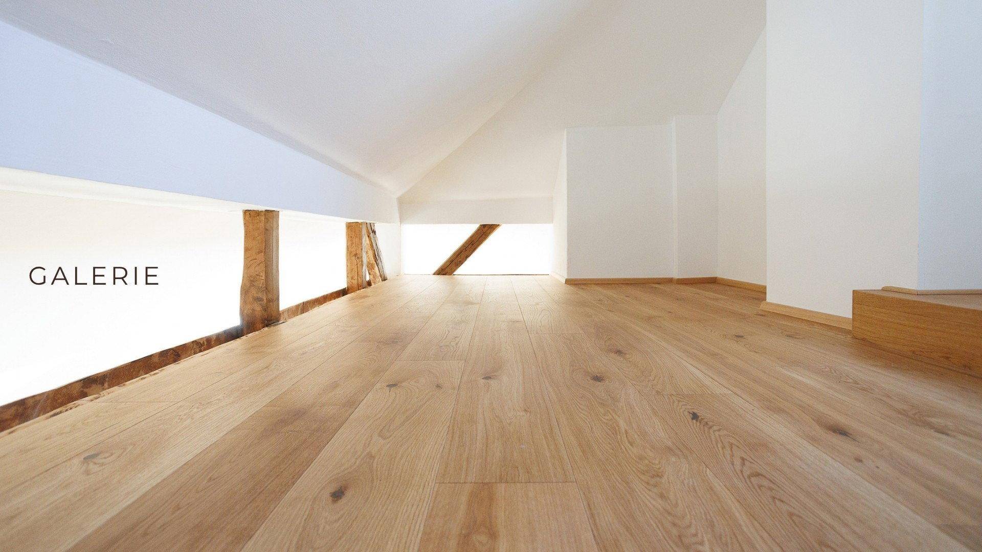 Helle Galerie mit Eichenparkettboden und sichtbaren Holzbalken, die einen offenen Wohnraum schafft.
