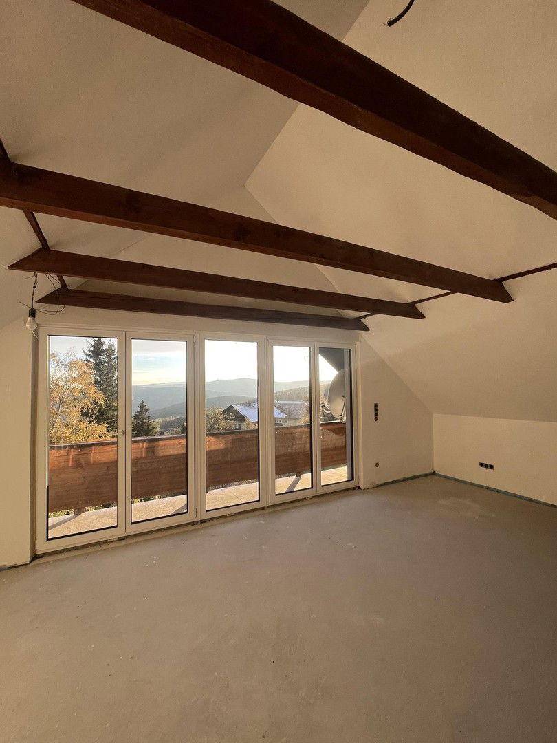 Geräumiger Raum im Dachgeschoss mit Holzbalken, großen Fenstern und weitem Bergblick.