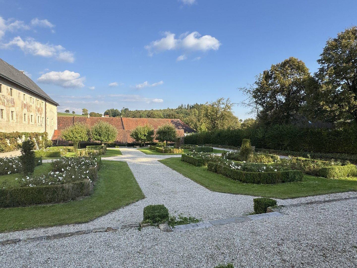 Weitläufiger formaler Garten mit gepflegten Hecken, Kieswegen und historischen Gebäuden im Hintergrund.