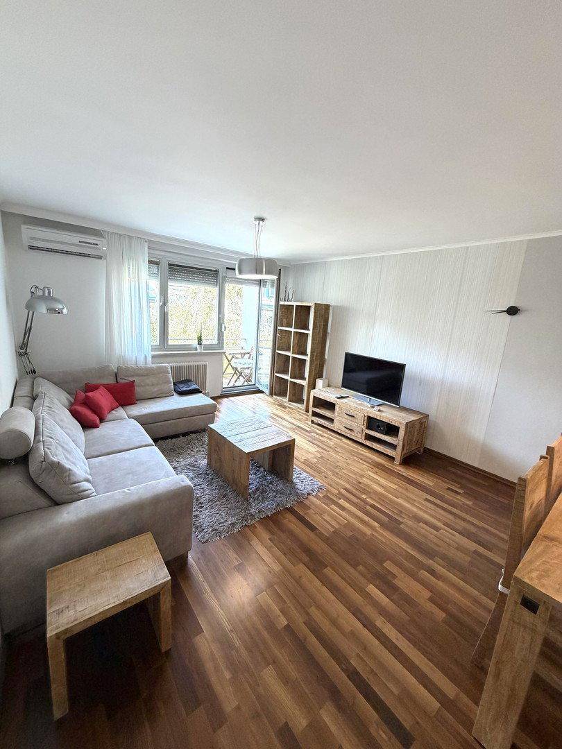Gemütliches Wohnzimmer mit Ecksofa, Holzboden und Klimaanlage, mit Zugang zum Balkon.