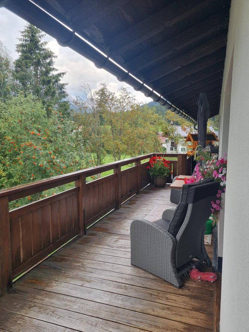 Gemütlicher Holzbalkon mit Sitzgelegenheiten und Blick auf die umliegende grüne Landschaft.