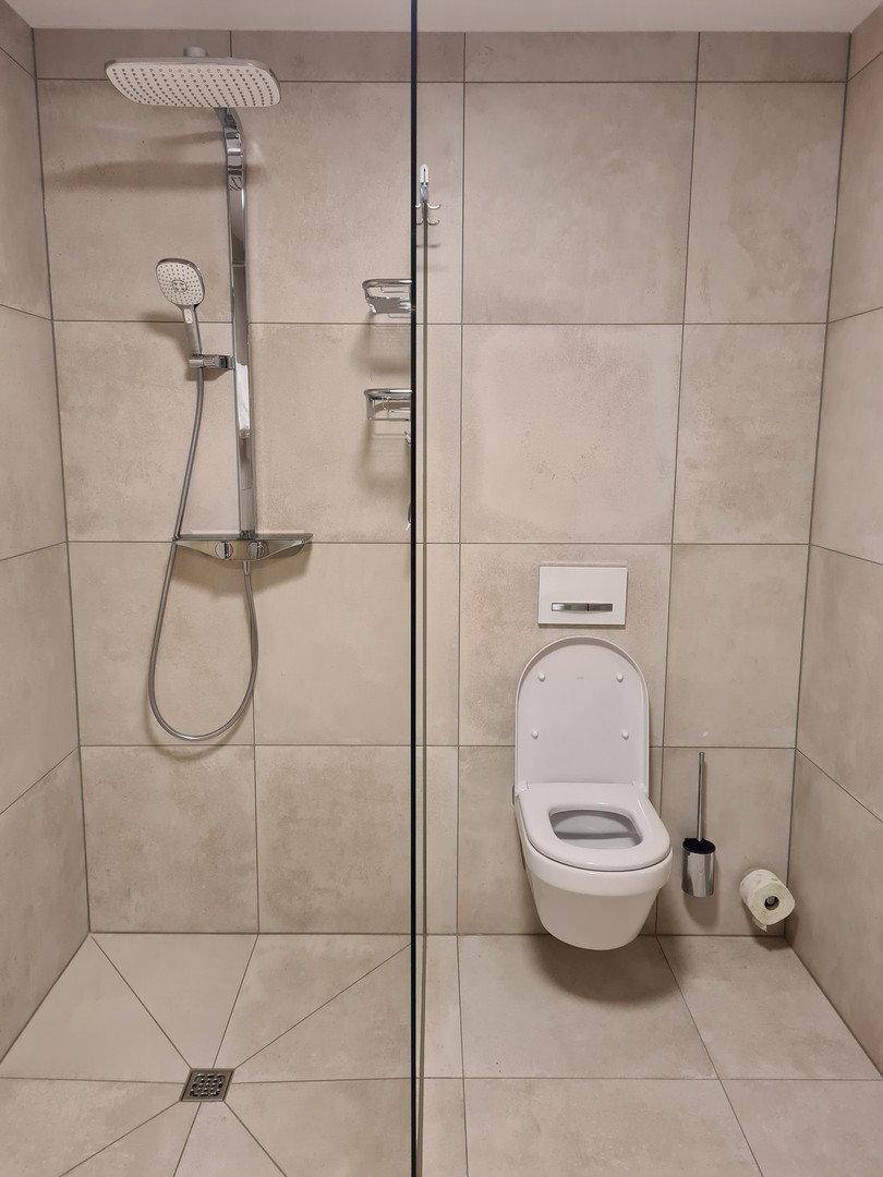 Helles Badezimmer mit ebenerdiger Dusche, Wand-WC und modernen Fliesen an Wänden und Boden.