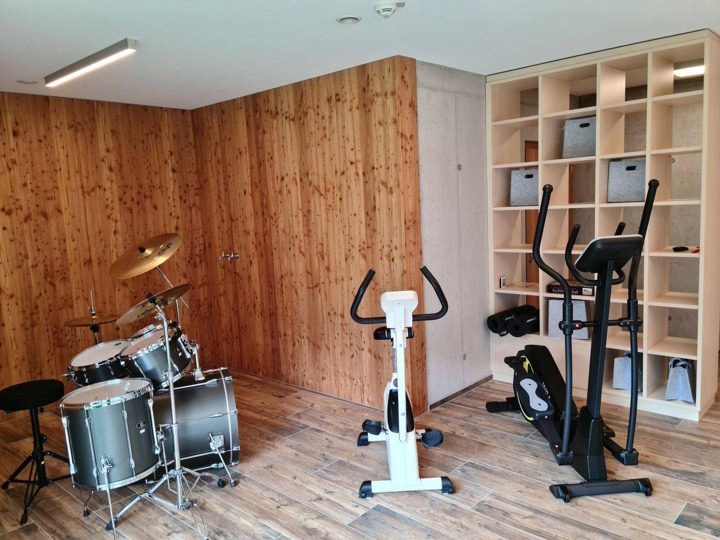 Fitnessraum mit Trainingsgeräten, Schlagzeug und integriertem Regal für Stauraum.