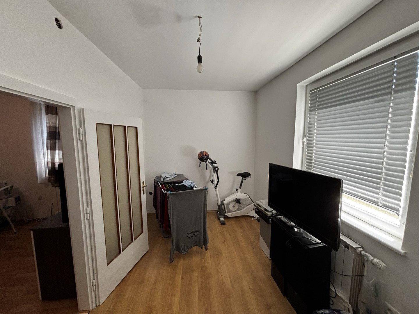Heller Raum mit Fenster, TV-Möbeln und einem Heimtrainer.
