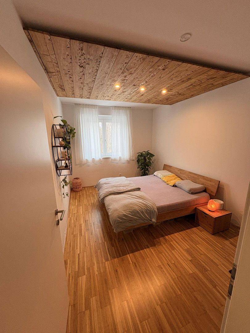 Schlafzimmer mit Holzboden, Holzakzentdecke und einem großen Fenster für viel Licht.