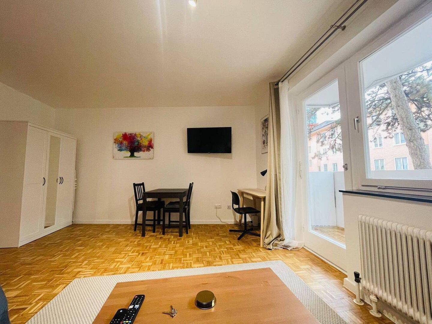 Geräumiger Wohnbereich mit Essplatz, Schreibtisch und Kleiderschrank, mit Balkonzugang.