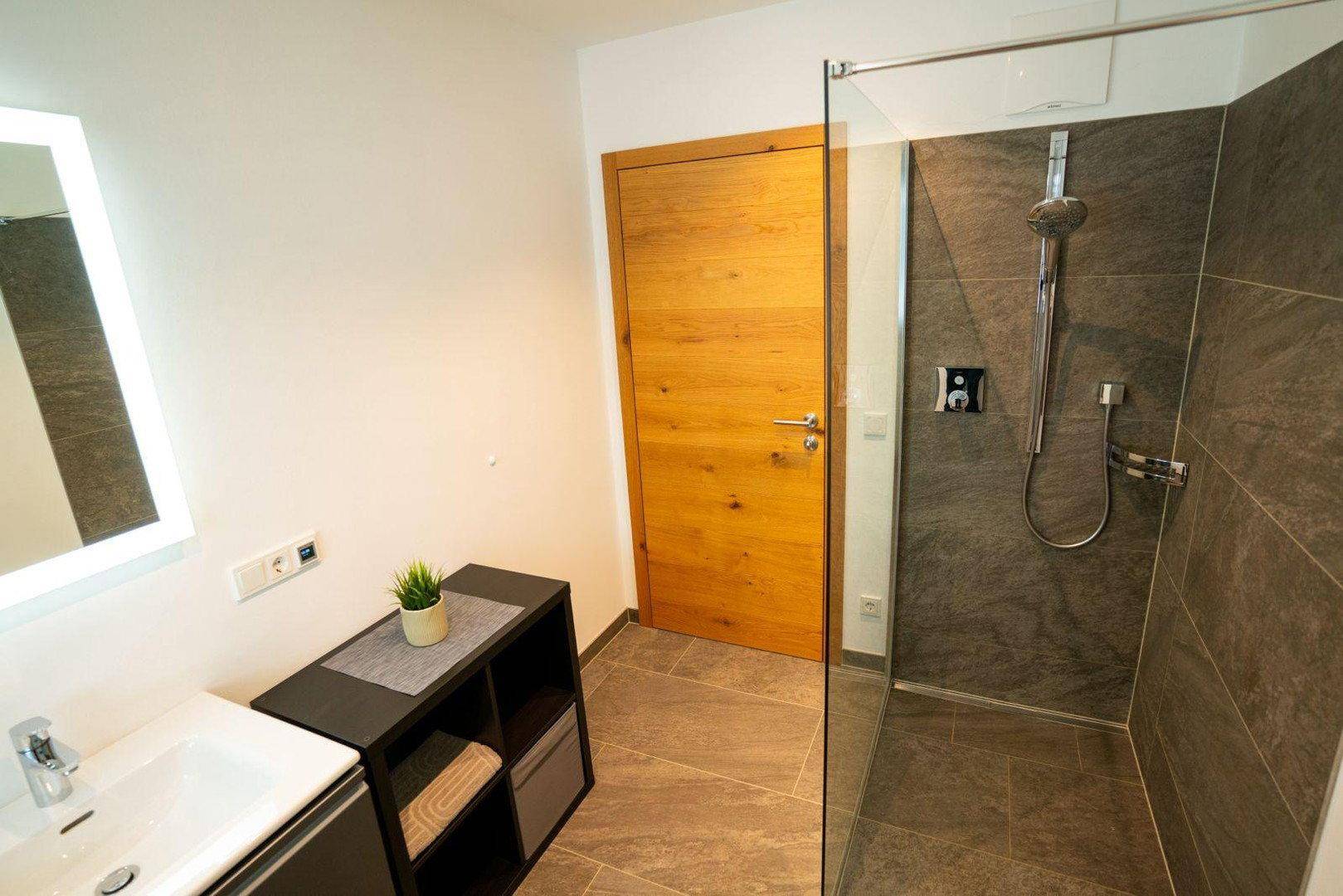 Modernes Badezimmer mit begehbarer Dusche und beleuchtetem Spiegel über dem Waschbecken.