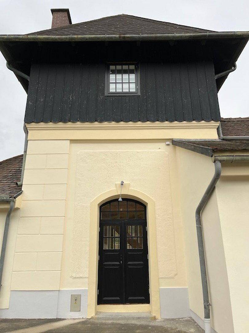 Historisches Gebäude mit dunkler Holzverkleidung im oberen Bereich und cremefarbener Fassade.