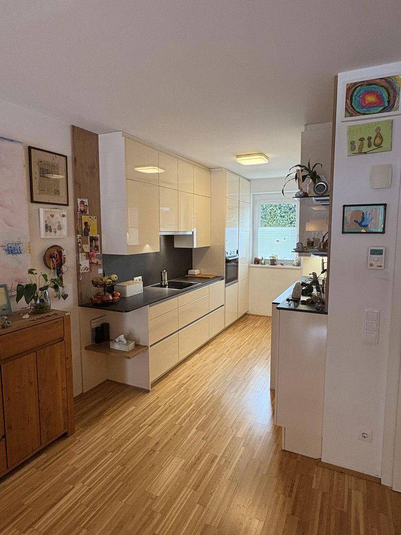 Moderne Küche mit hellen Hochglanzfronten, dunkler Arbeitsplatte und Holzboden.