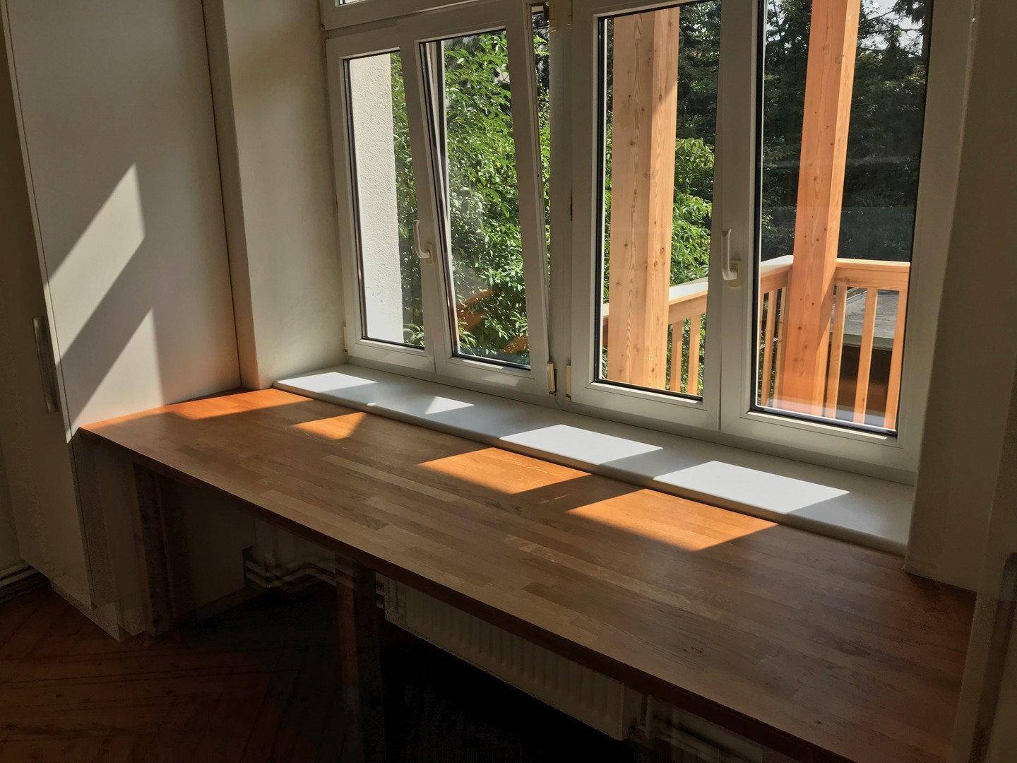 Detailansicht der Holz-Arbeitsplatte unter dem großen Fenster, das den Raum mit Sonnenlicht füllt.