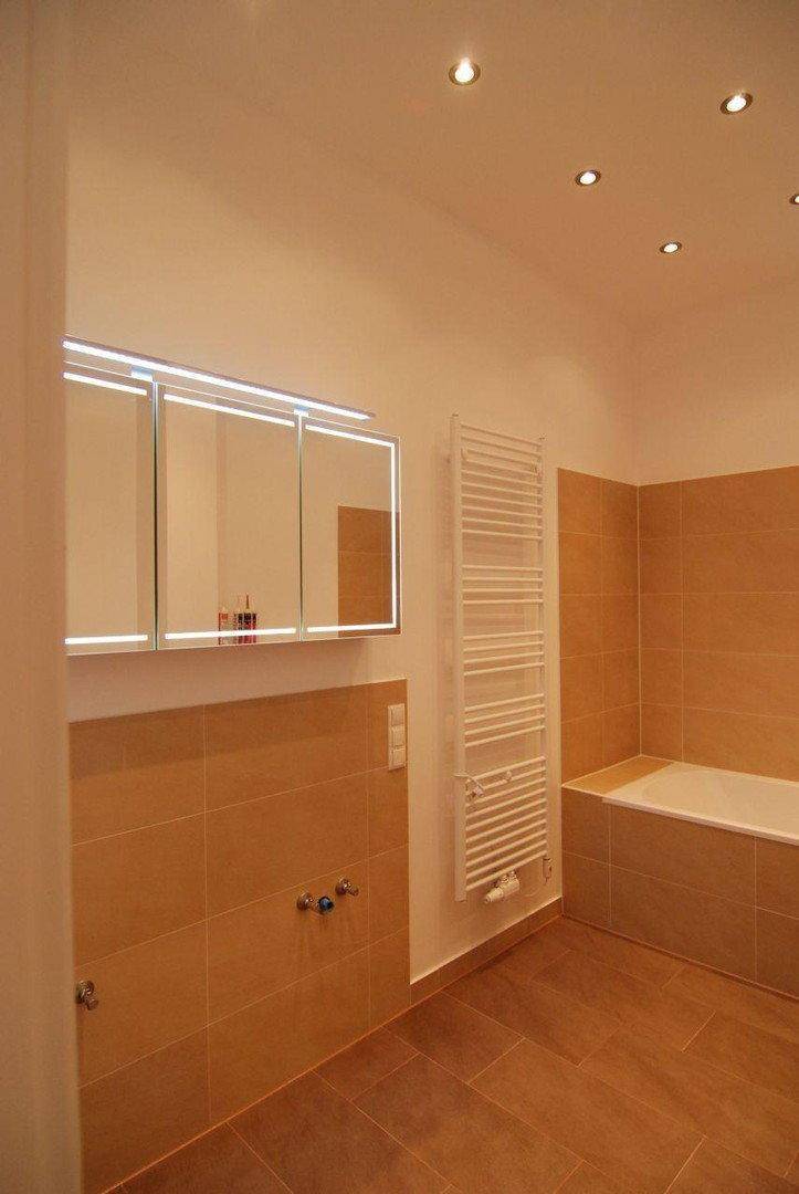 Funktionales Badezimmer mit Spiegelschrank, beheiztem Handtuchhalter und beigefarbenen Fliesen.