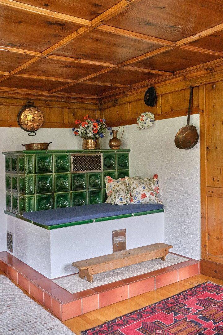 Traditioneller grüner Kachelofen mit Sitzbank und rustikalen Dekorationen in einem Holzinterieur.