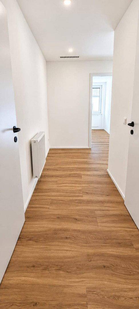 Langer, heller Flur mit modernem Laminatboden und weiß gestrichenen Wänden, der zu weiteren Räumen führt.