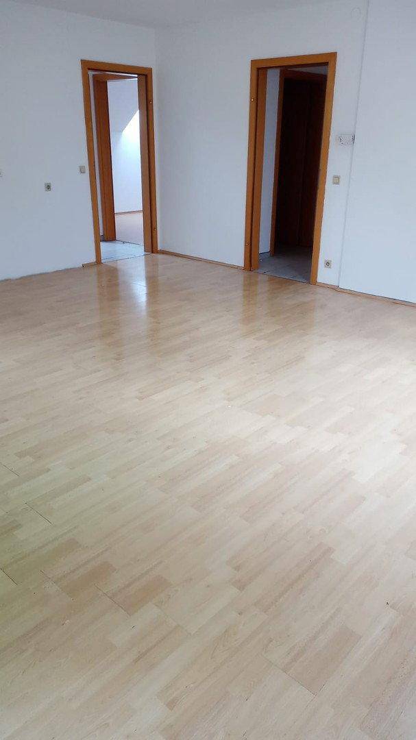 Geräumiger, heller Raum mit Holzboden und zwei Türöffnungen, der vielseitig nutzbar ist.