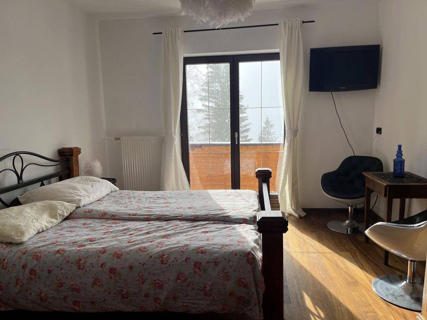 Schlafzimmer mit Doppelbett, Holzboden, Fernseher und Balkonzugang mit Winterblick.