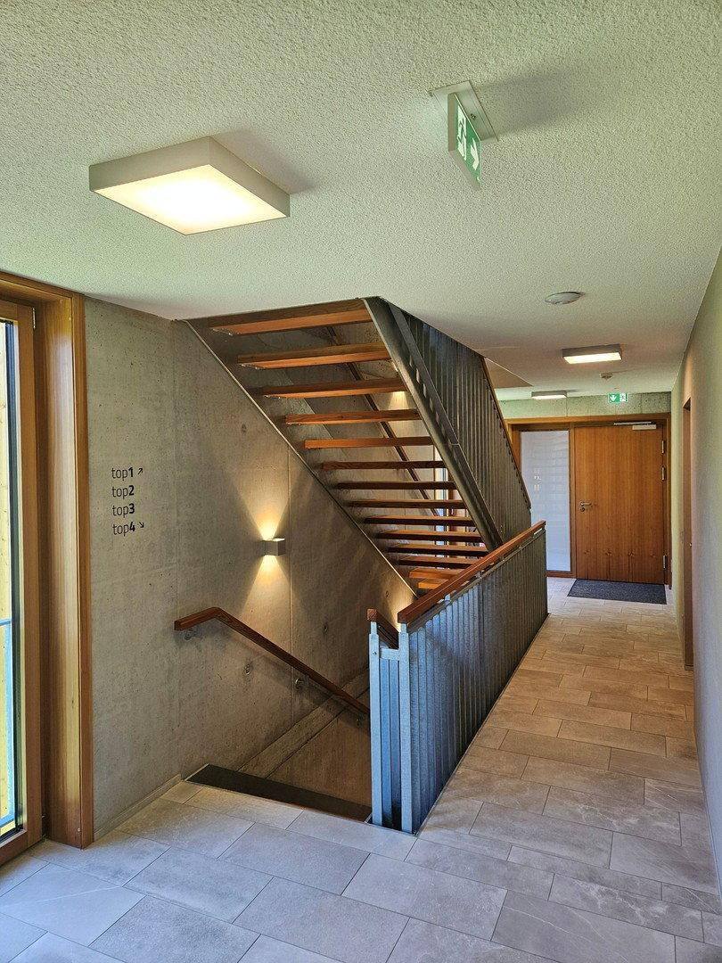 Heller Treppenaufgang mit Holzstufen, Metallgeländer und Sichtbetonwänden im modernen Stil.