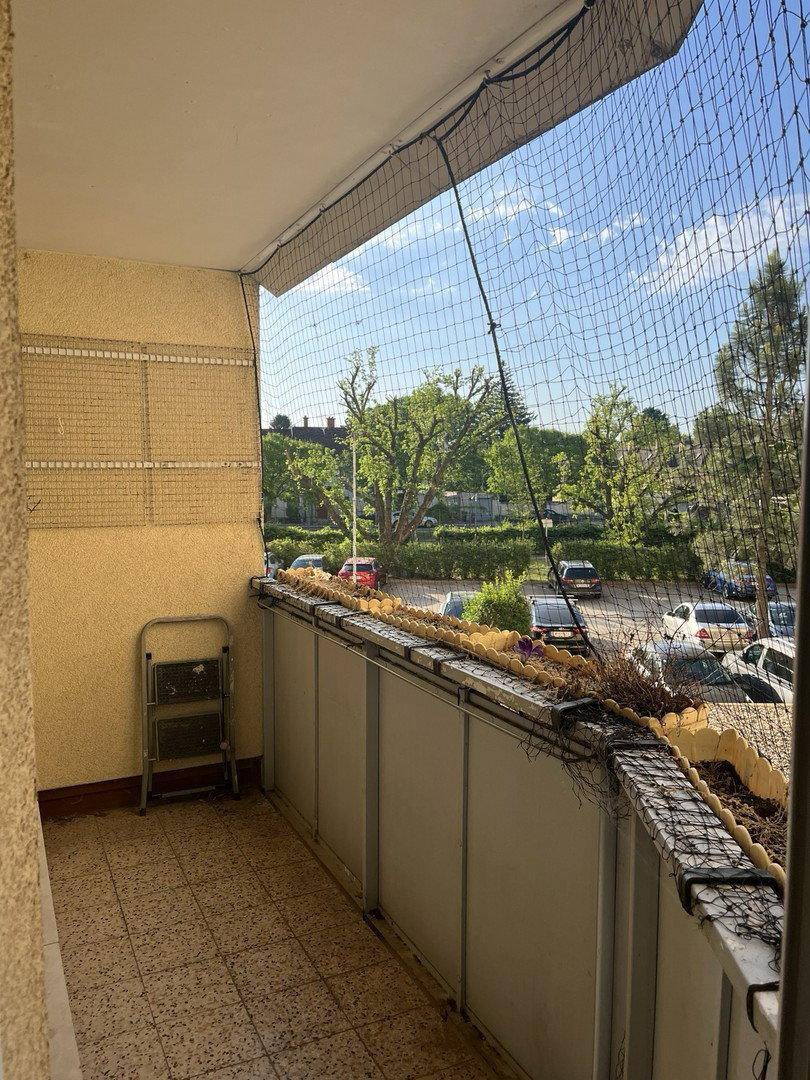 Balkon mit Fliesenboden, Sicherheitsnetz und Blick auf Bäume sowie parkende Autos.