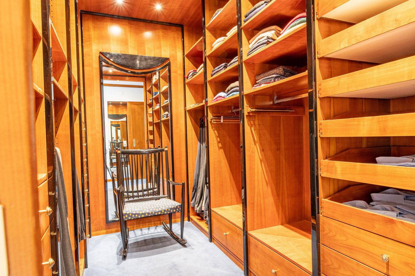 Geräumiger begehbarer Kleiderschrank mit Holzregalen, Spiegel und Teppichboden.