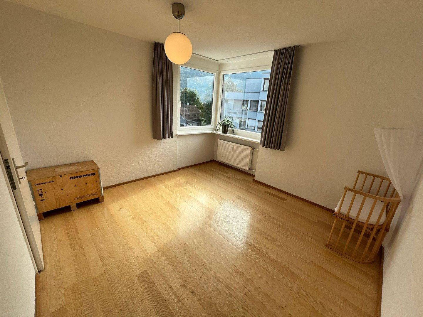 Helles Zimmer mit Holzboden, großen Fenstern und einem Kinderbett, ideal als Kinderzimmer.