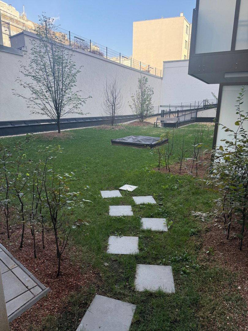 Gemeinschaftlicher Gartenbereich mit Rasenfläche, jungen Bäumen und Gehwegen.