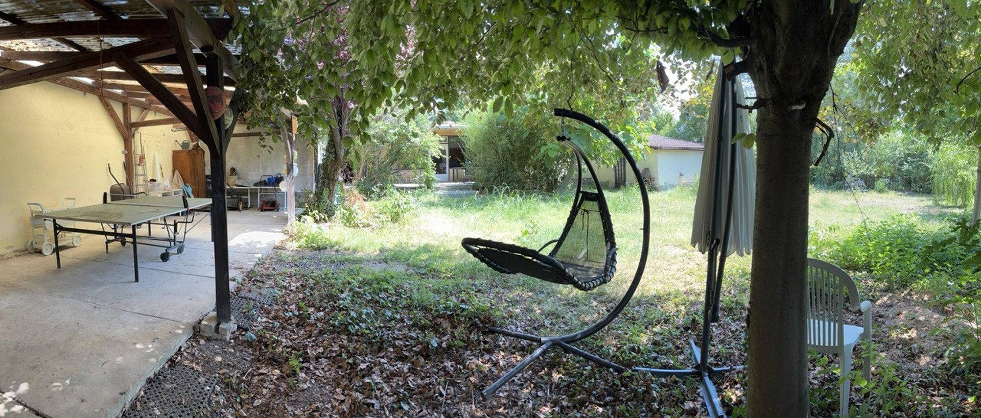 Entspannungsbereich im Garten mit Hängesessel und Tischtennisplatte unter einem Vordach.