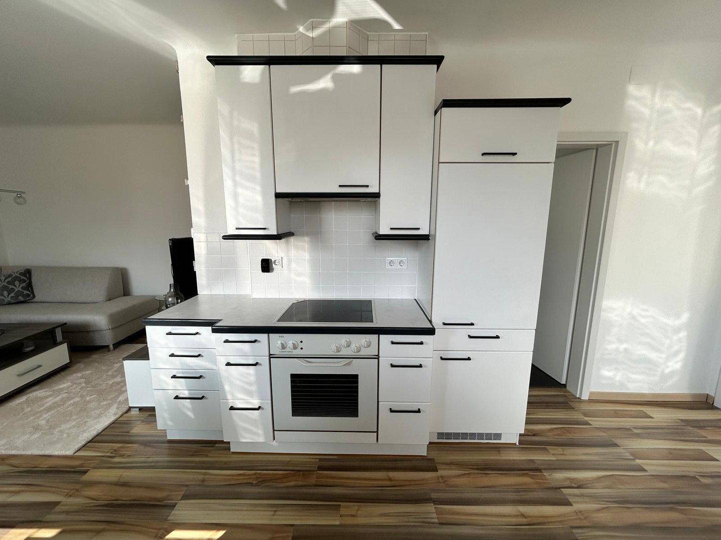 Moderne Einbauküche mit weißen Schränken, Backofen und Kochfeld im offenen Wohnbereich.
