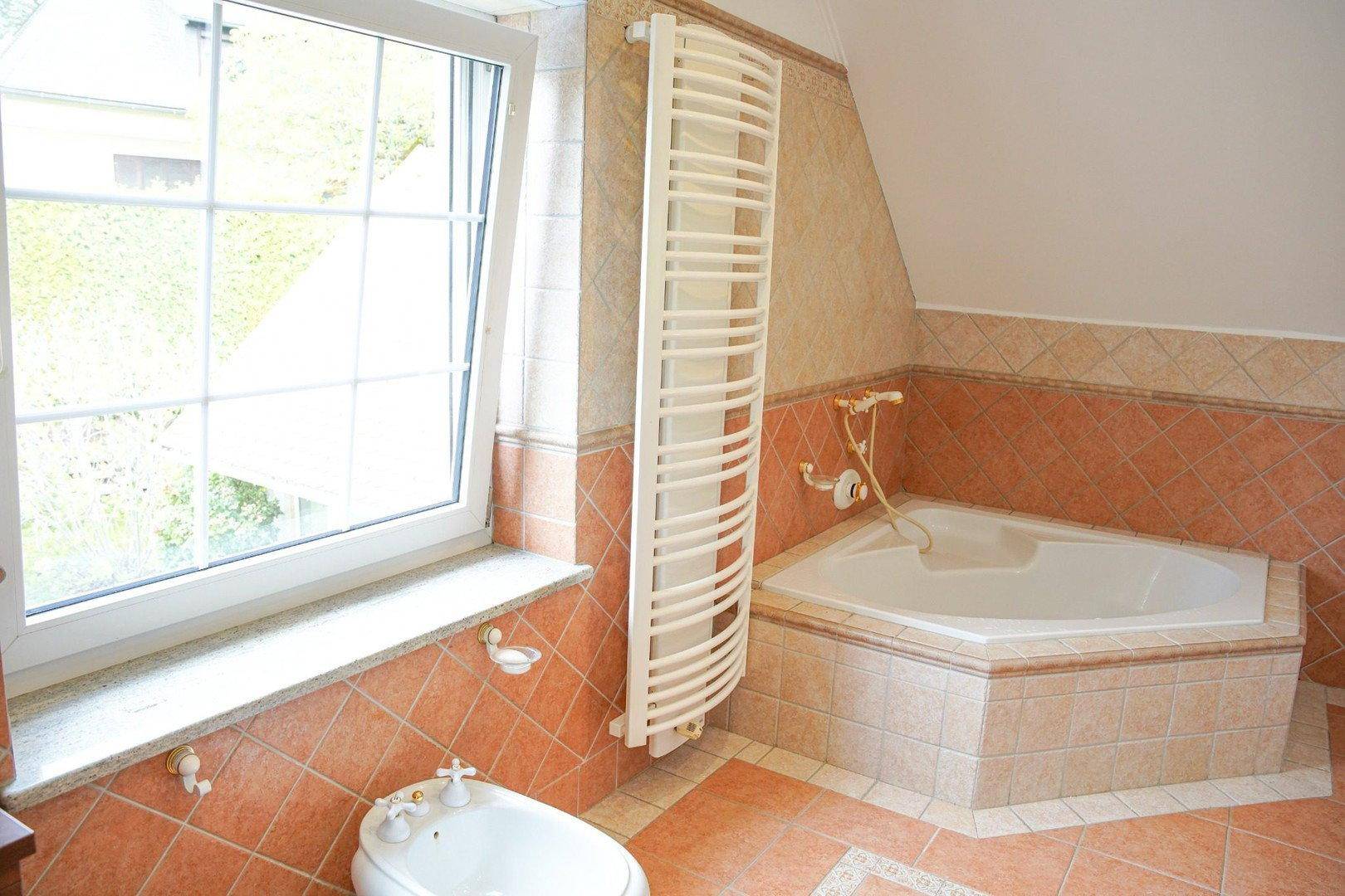 Badezimmer mit Eckbadewanne, Bidet, Fenster und Handtuchheizkörper.