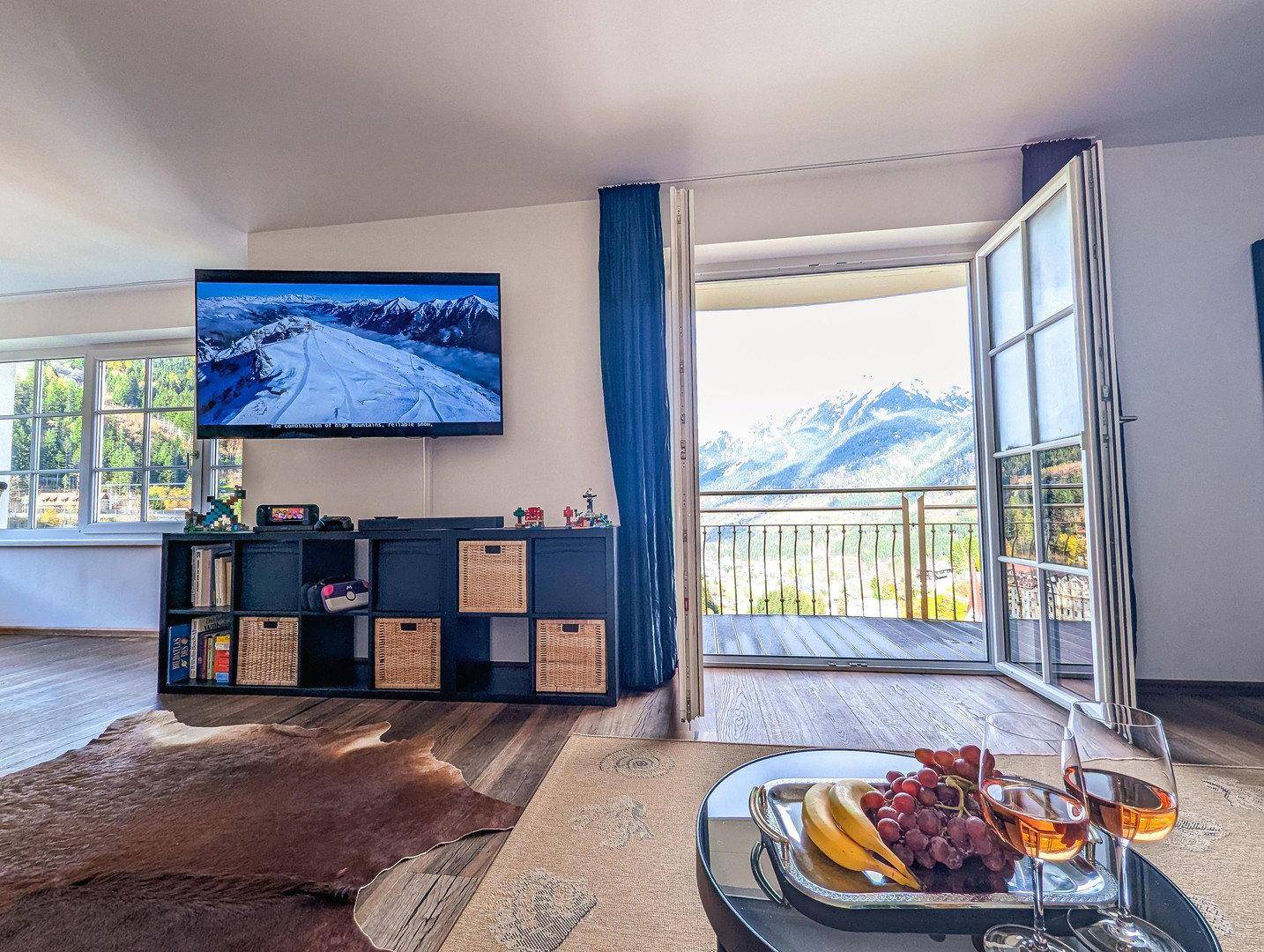 Gemütlicher Wohnbereich mit Fernseher, Holzboden und direktem Zugang zum Balkon mit Bergblick.