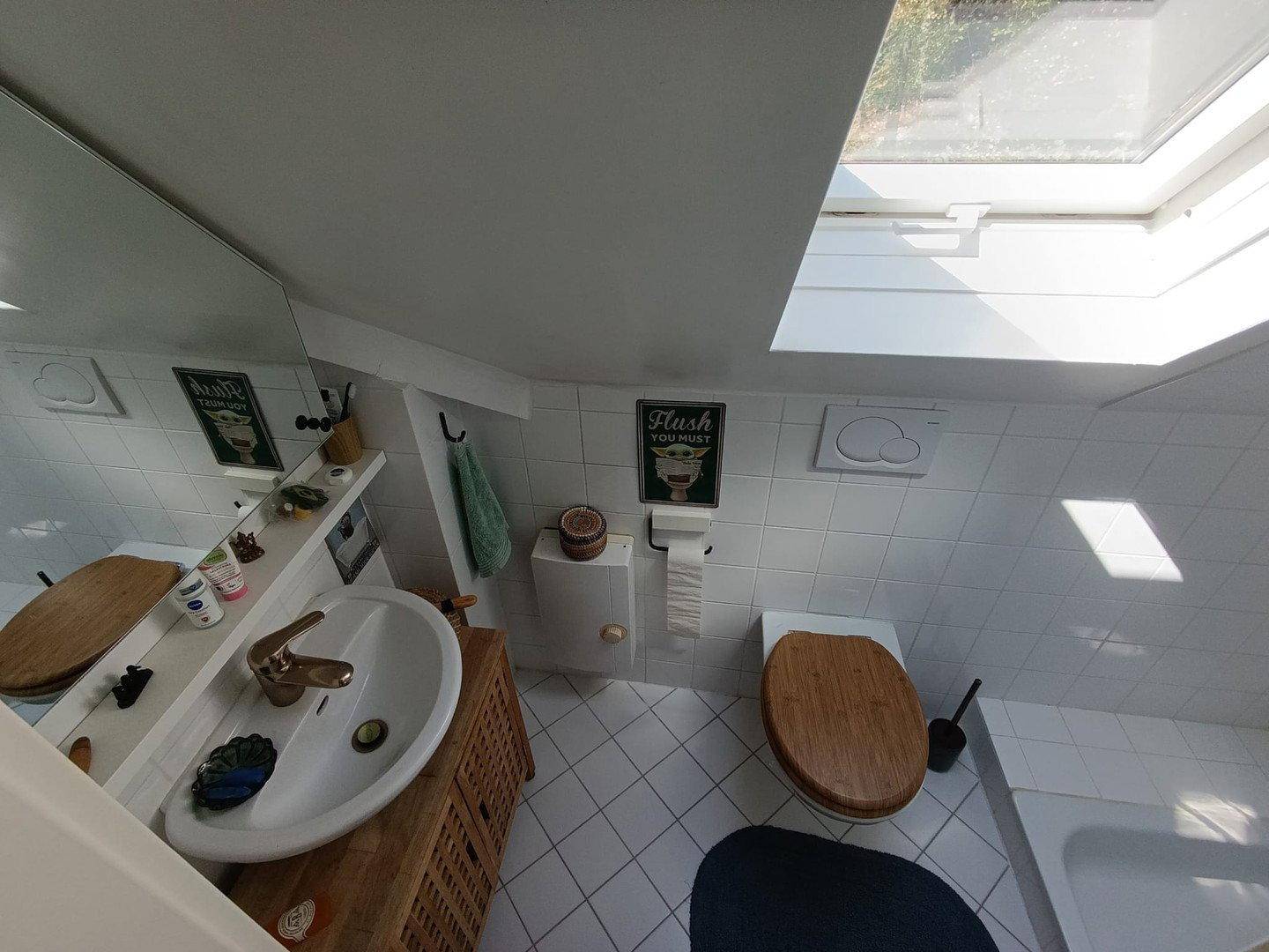 Badezimmer mit Dachfenster, weißen Fliesen, Holzwaschtisch und WC mit Holzdeckel.