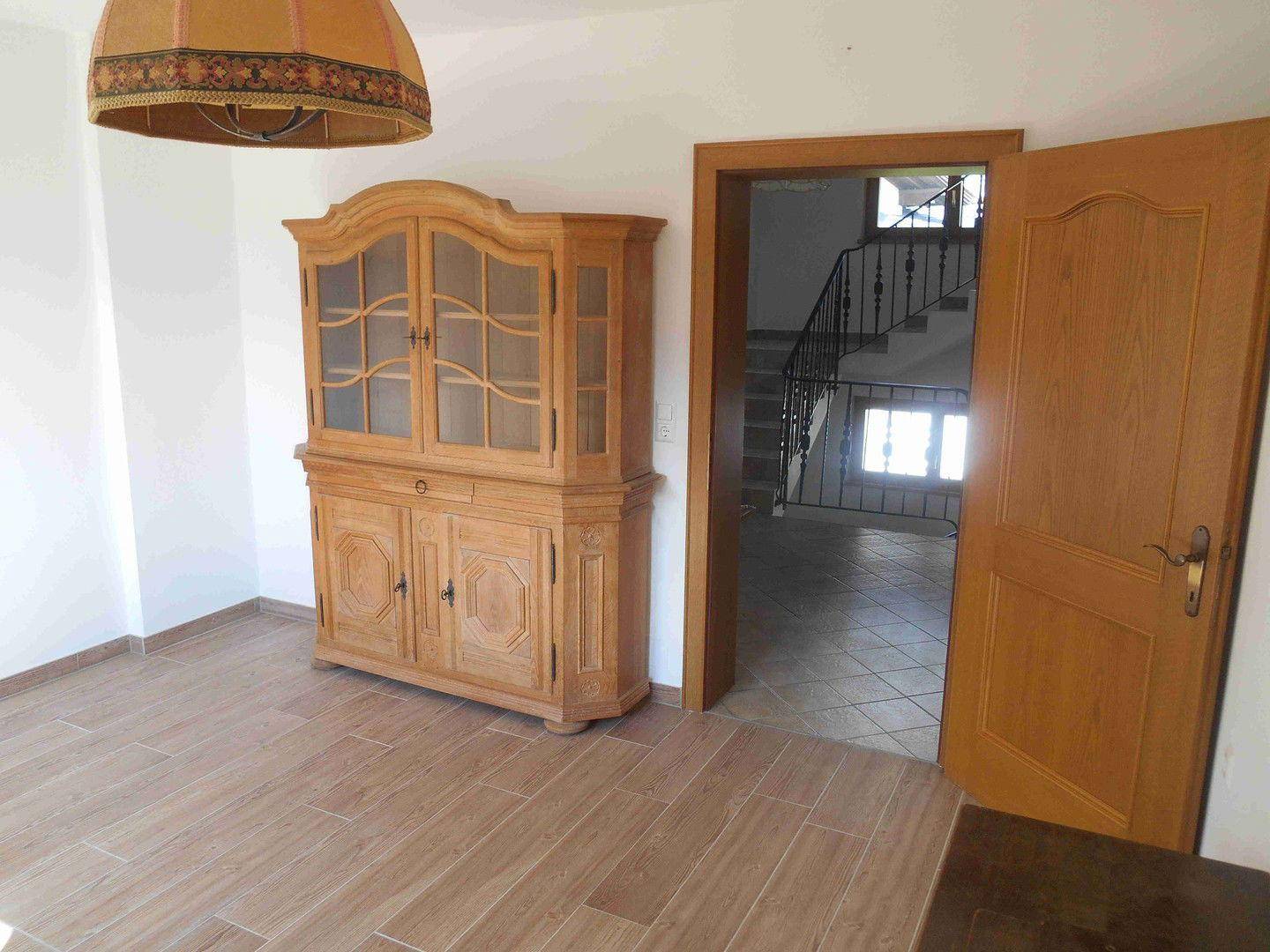 Heller Raum mit Fliesenboden, traditionellem Holzschrank und Blick auf die Treppe.