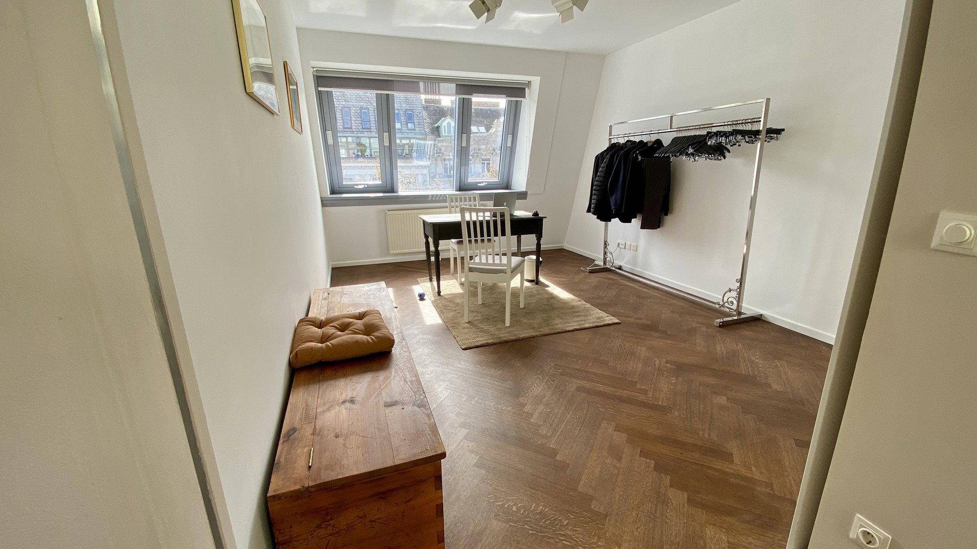 Vielseitiger Raum mit Holzboden, Tisch und Kleiderstange, ideal als Arbeits- oder Gästezimmer.