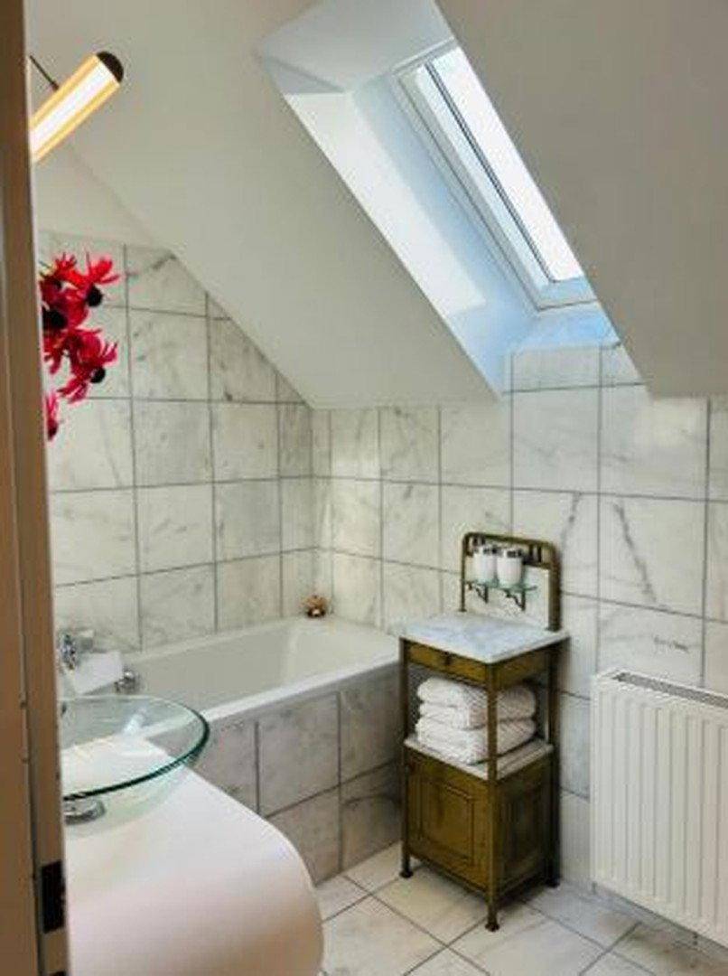 Helles Badezimmer mit Marmorfliesen, Badewanne, Heizkörper und einem Dachfenster.