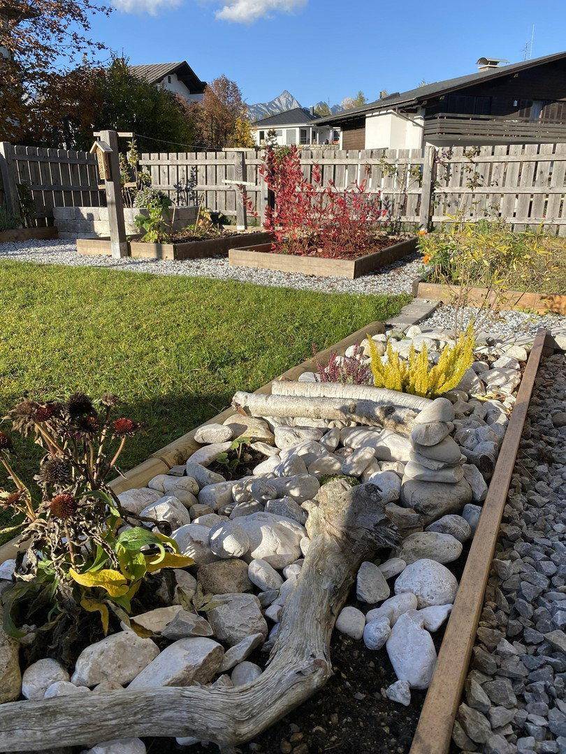 Gepflegter Garten mit Hochbeeten, Steinelementen und Rasenfläche.