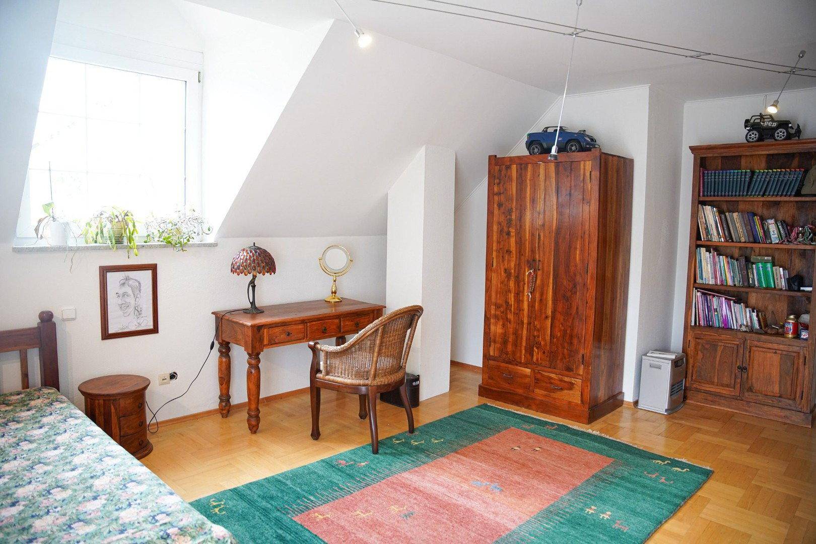 Gemütliches Schlafzimmer im Dachgeschoss mit Einzelbett, Schreibtisch und Holzschrank, unter der Dachschräge.