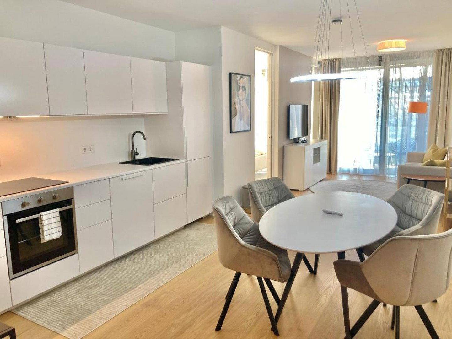Offener Wohn-Essbereich mit moderner Küche, Esstisch und Zugang zum Balkon.