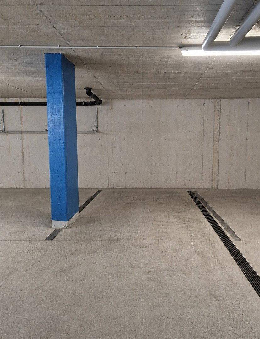 Leerer Stellplatz in einer Tiefgarage mit Betonwänden und blauen Säulen.