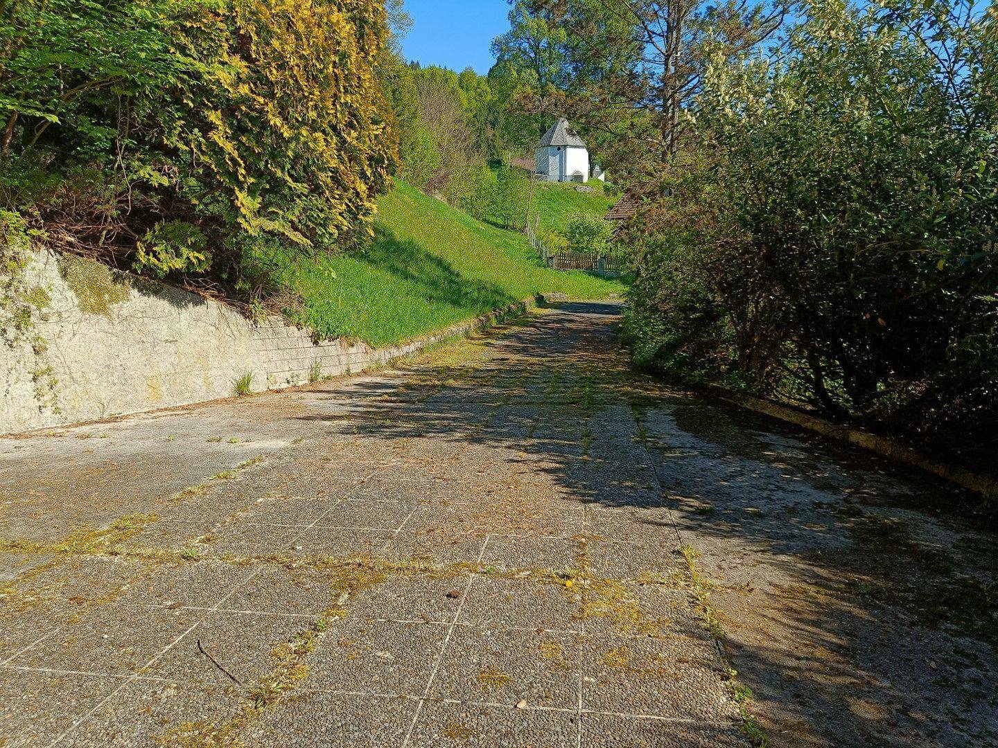 Breite gepflasterte Auffahrt oder Weg führt einen grünen Hang hinauf zu einem Gebäude.