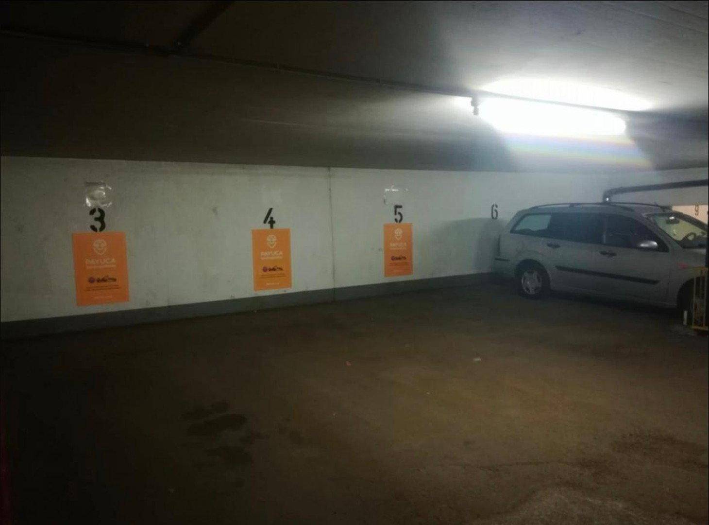 Tiefgarage mit nummerierten Stellplätzen und einem geparkten Fahrzeug an der Wand mit Werbung.