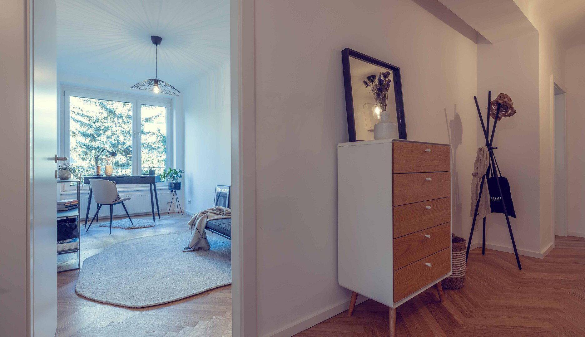 Blick vom Flur in ein helles Zimmer mit Schreibtisch, Teppich und großem Fenster.