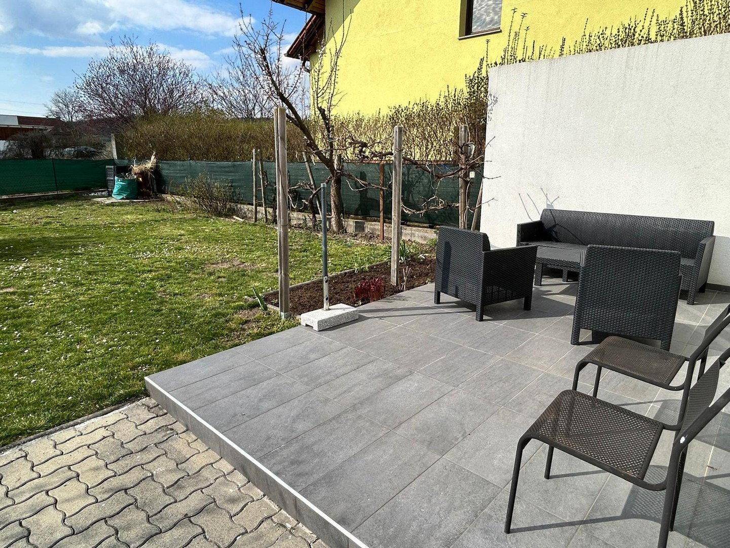 Gepflegter Garten mit Rasenfläche, gepflasterter Terrasse und modernen Outdoor-Sitzmöbeln.