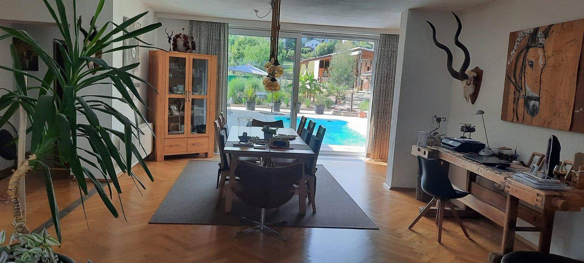 Heller Essbereich mit großem Holztisch, Parkettboden und direktem Blick auf den Außenpool.